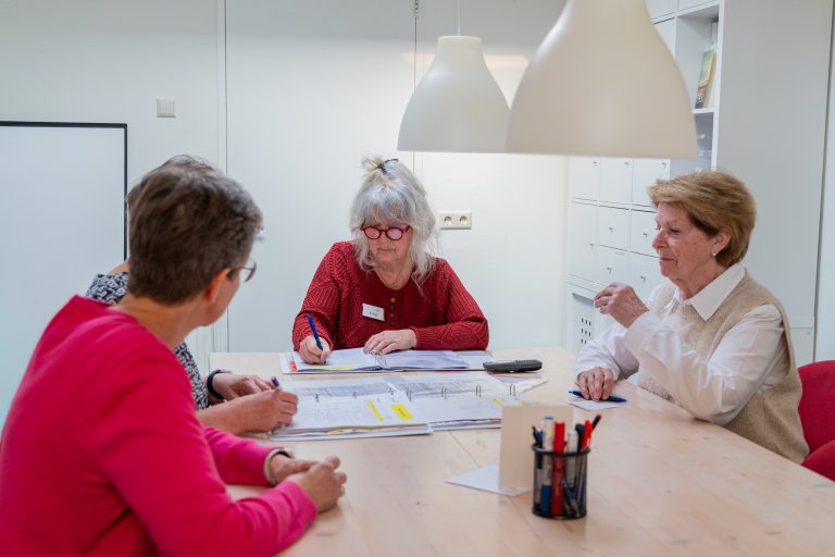 Vier personen aan een tafel waar diverse mappen op liggen